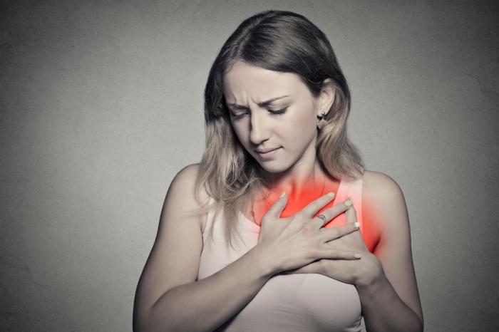 Image of a young woman in pain who is holding her hands over her chest due to GERD-related heartburn