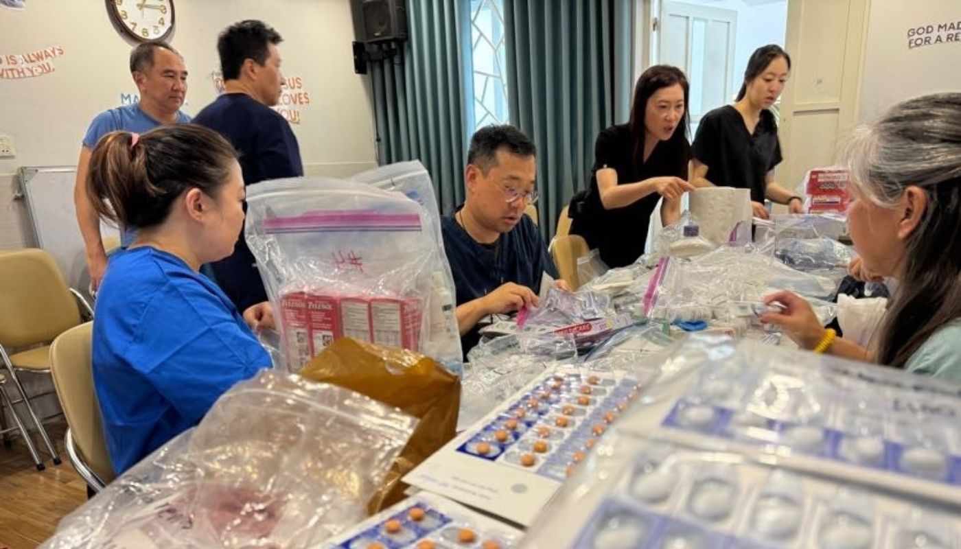 People organizing a large stack of medications on a table. 
